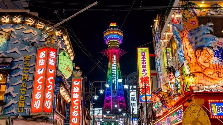 Quartiere Shinsekai a Osaka di notte con la Tsutenkaku illuminata, insegne luminose e atmosfera vivace della nightlife cittadina, vicino alle zone frequentate dalla comunit&agrave; LGBTQ+
