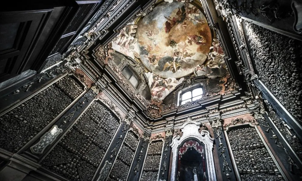 Interno della Chiesa di San Bernardino alle Ossa a Milano, famosa per la sua cappella decorata con ossa umane. Le pareti rivestite di teschi e tibie creano un&rsquo;atmosfera suggestiva, mentre l&rsquo;affresco barocco sul soffitto aggiunge un tocco di solennit&agrave; e mistero a questo luogo storico e unico.