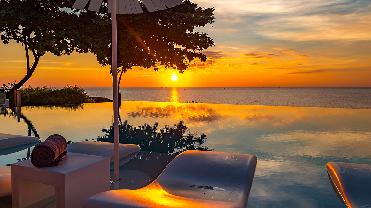Tramonto mozzafiato su infinity pool a Phuket, Thailandia, con sdraio bianche e mare calmo all&rsquo;orizzonte. Atmosfera rilassante e colori caldi del sole che si riflettono sull&rsquo;acqua.