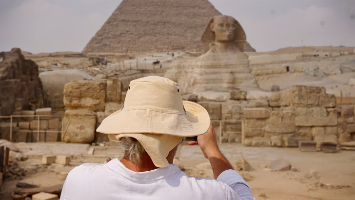 Luigi di Gayly Planet con cappello da safari mentre fotografa la Sfinge e la Piramide di Giza in Egitto. Viaggio alla scoperta delle meraviglie dell&rsquo;Antico Egitto con consigli su cosa mettere in valigia per affrontare il clima desertico.