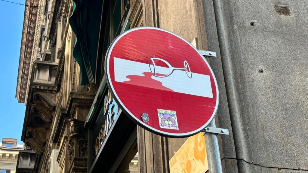 Segnale stradale modificato dall&rsquo;artista Clet Abraham nel centro di Milano. Il cartello di divieto d&rsquo;accesso &egrave; stato trasformato con un&rsquo;illustrazione di un bicchiere rovesciato che versa vino, un esempio di street art ironica e creativa che caratterizza molte citt&agrave; europee.