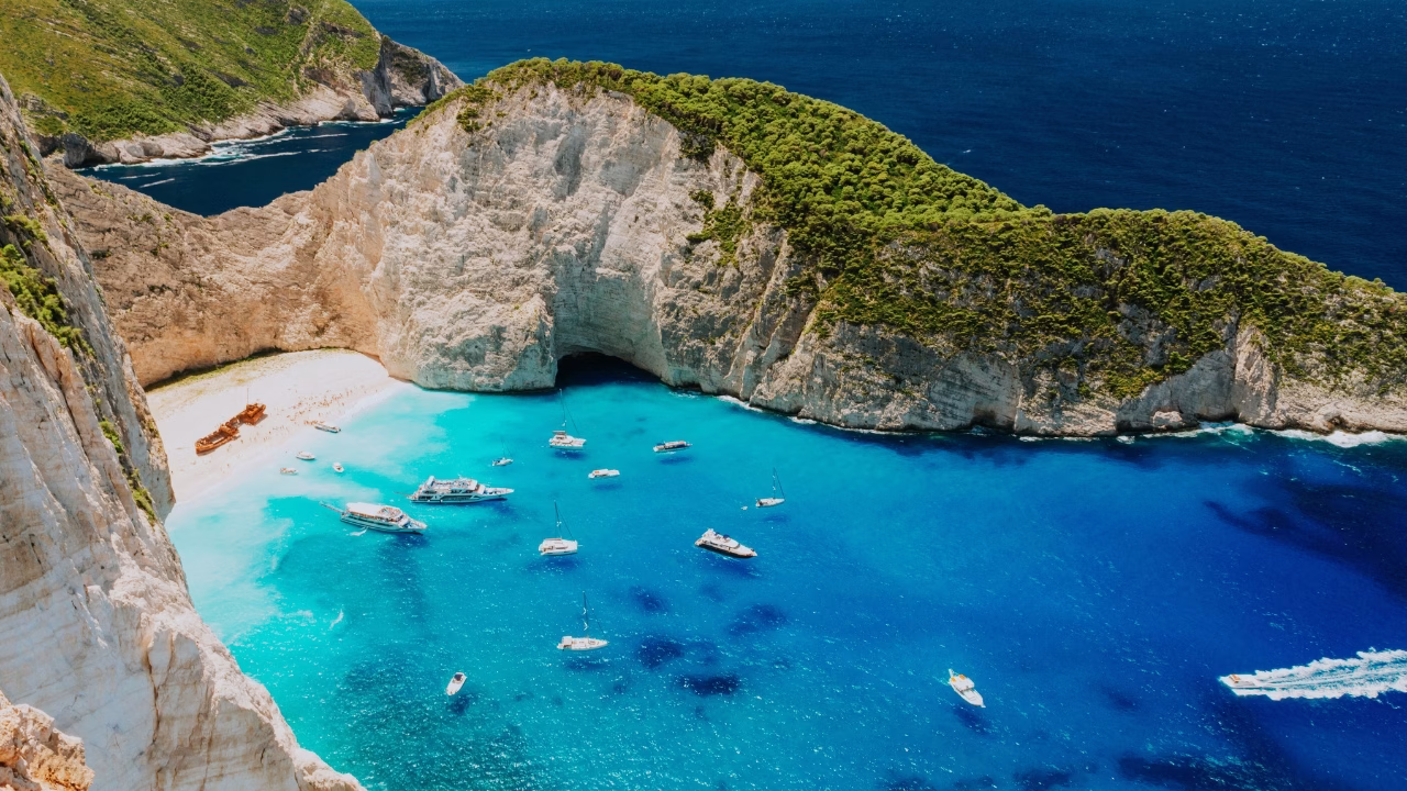 Spiaggia del Relitto o Navagio di Skiathos gay con acqua cristallina, barche ormeggiate e spiaggia dorata circondata da alte scogliere bianche.