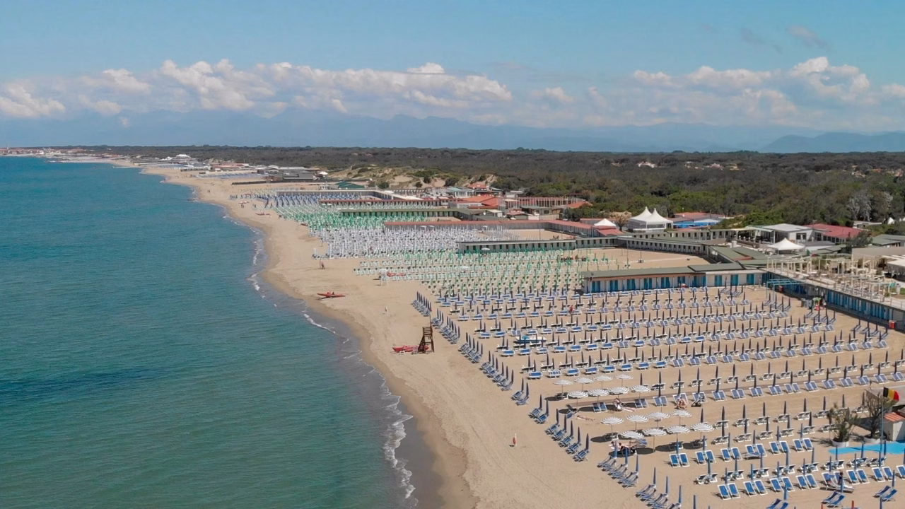 Veduta aerea della spiaggia di Tirrenia in Toscana con file ordinate di ombrelloni e lettini, una delle mete gay friendly e nudiste pi&ugrave; frequentate della costa tirrenica.