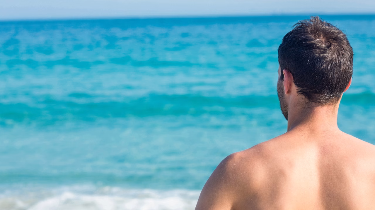 Uomo di spalle che guarda il mare turchese dalla spiaggia gay e naturista di Gabicce Mare sulla riviera romagnola.