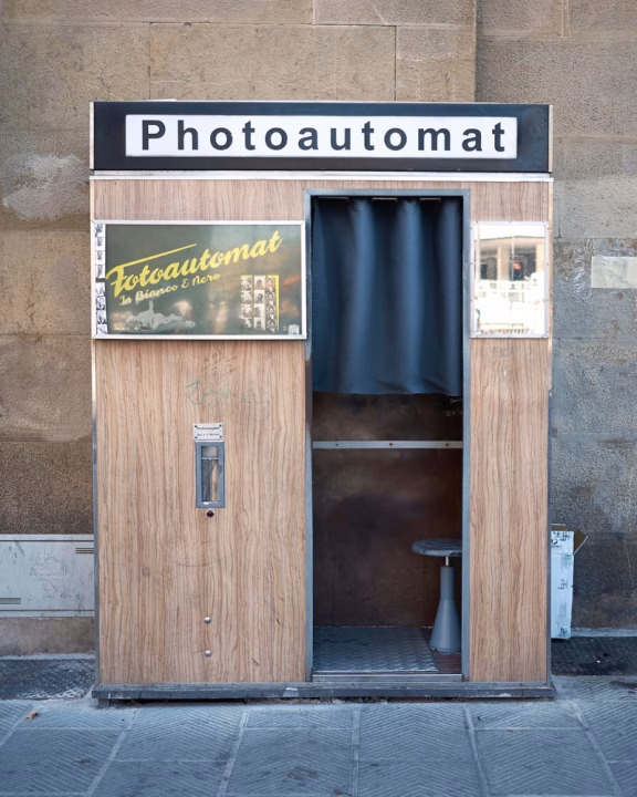 Cabina per fototessere vintage &ldquo;Photoautomat&rdquo; a Firenze, con struttura in legno e tenda scura, che offre foto in bianco e nero in stile analogico. Un angolo nostalgico e retr&ograve; nel cuore della citt&agrave;.