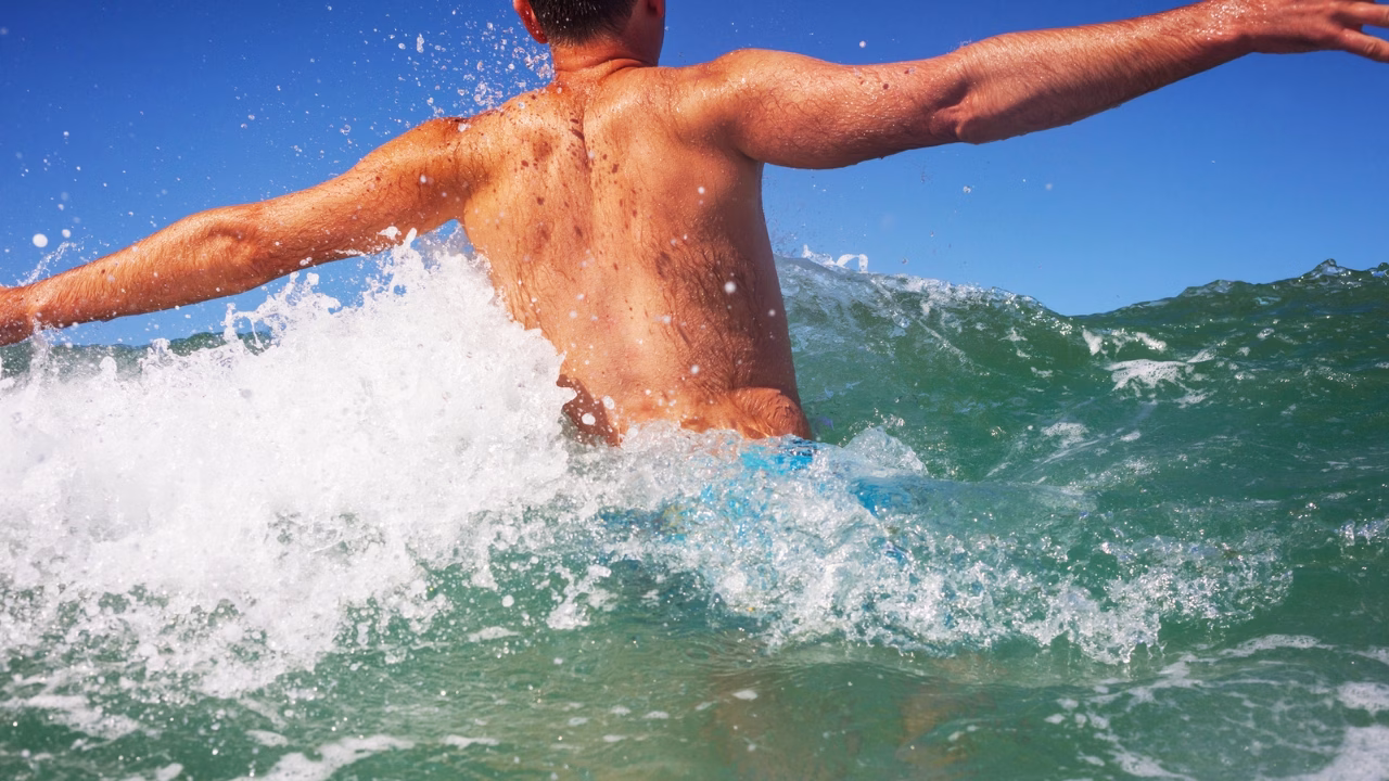 Uomo che nuota tra le onde in una spiaggia della costiera amalfitana, meta ideale per il turismo LGBTQ+ e per chi cerca spiagge gay-friendly in Campania con panorami mozzafiato.