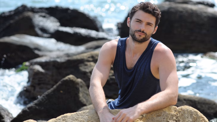 Giovane uomo seduto su una roccia in riva al mare con sfondo roccioso, in una delle spiagge gay e naturiste dell&rsquo;Abruzzo, meta LGBTQ+ per chi cerca tranquillit&agrave;, bellezza naturale e turismo inclusivo lungo la costa abruzzese.