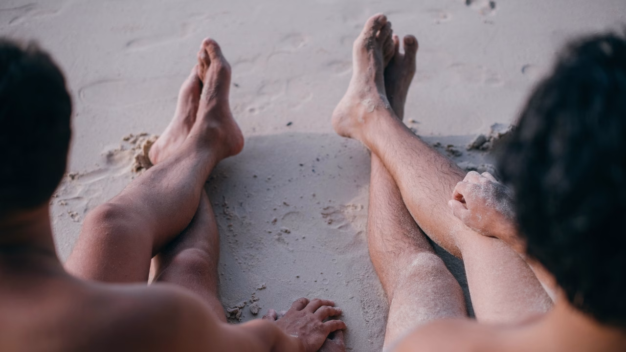 Coppia gay rilassata sulla sabbia di una spiaggia LGBTQ+ a Salerno, una delle destinazioni pi&ugrave; apprezzate per chi cerca spiagge gay-friendly e naturiste in Campania.