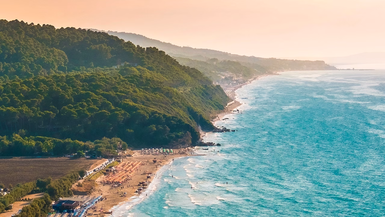Veduta aerea della spiaggia delle Murgette nel Gargano, con mare turchese e pineta rigogliosa che si estende lungo la costa, destinazione popolare tra i turisti e frequentata dalla comunit&agrave; LGBTQ+