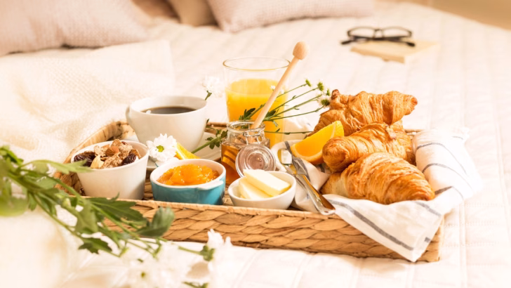 Colazione a letto con croissant, marmellata, burro, miele, succo d&rsquo;arancia e caff&egrave;, servita su un vassoio in una camera d&rsquo;hotel accogliente. Un&rsquo;esperienza perfetta per un soggiorno in hotel particolari e romantici in Lombardia.
