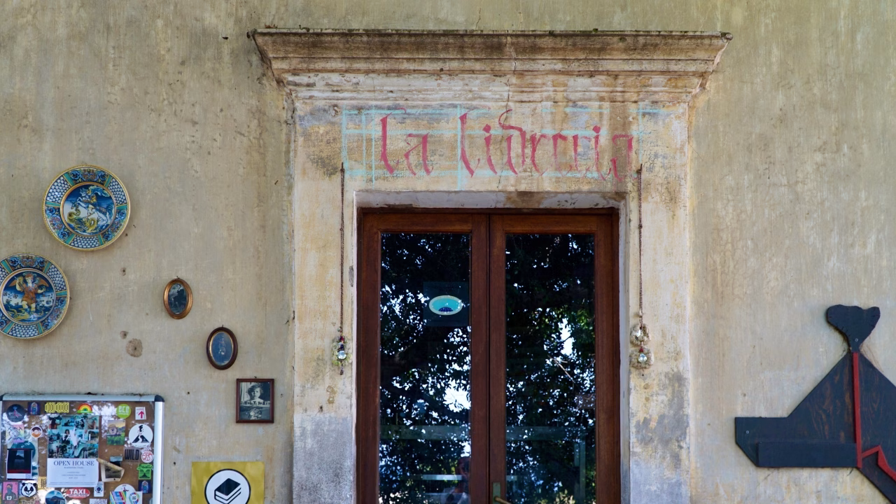 L&rsquo;ingresso de la libreria Stromboli con una porta in legno e vetro, con il nome &ldquo;La Libreria&rdquo; scritto sopra. Il muro esterno, decorato con piatti di ceramica e piccoli quadri, conferisce un fascino rustico e accogliente.