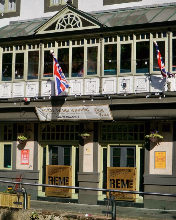 Ingresso del The Rembrandt Hotel, hotel gay con bar LGBTQ+ Rem Bar nel cuore del Gay Village di Manchester, con bandiere britanniche e insegna &ldquo;Pub of the Year&rdquo;.