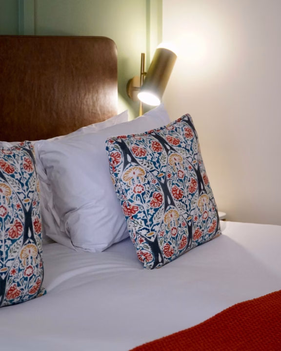Dettaglio della camera dell&rsquo;hotel gay friendly The Reach at Piccadilly a Manchester con cuscini decorati, testiera in pelle e luce da lettura moderna.
