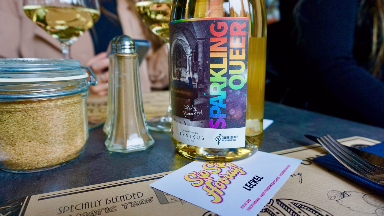Bottiglia di vino bianco con etichetta rainbow &ldquo;Sparkling Queer&rdquo; su un tavolo apparecchiato durante un gay brunch a Monaco di Baviera, in uno dei locali LGBTQ+ pi&ugrave; inclusivi e colorati della citt&agrave;.