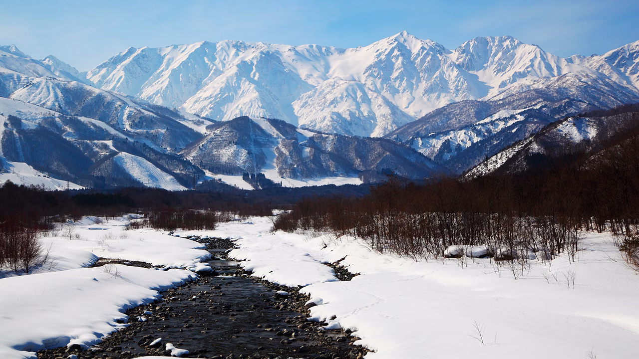 Panorama innevato del Gay Ski Week a Hakuba, con vista spettacolare sul Monte Shiroumadake a Nagano, Giappone, tra montagne maestose, piste da sci e un fiume che scorre tra la neve.