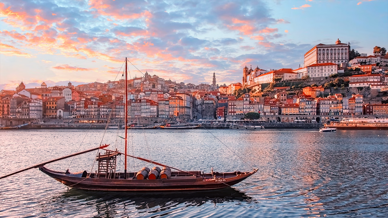 Vista panoramica sul centro storico di Porto al tramonto con barca tradizionale sul fiume Douro, perfetta per un viaggio gay autunnale in Portogallo.