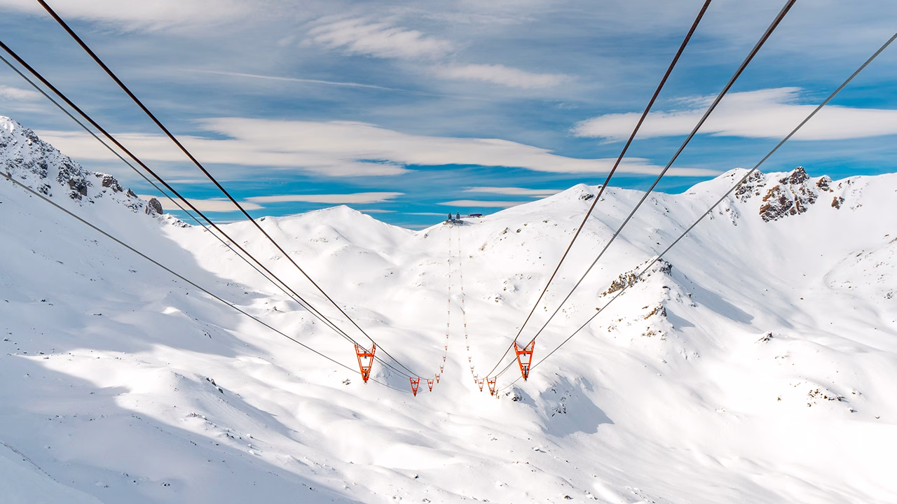 Vista panoramica delle piste innevate di Arosa durante la ski gay week in Svizzera, con impianti di risalita che attraversano le montagne sotto un cielo azzurro e nuvole leggere.
