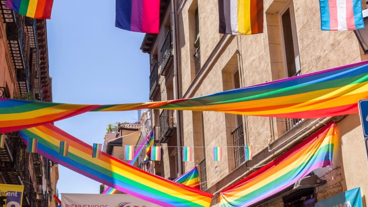 Strada di Torremolinos decorata con grandi bandiere arcobaleno e altre bandiere LGBTQIA+, tra cui quelle bisessuali, transgender e bear, appese tra i palazzi durante un evento Pride a Torremolinos. L&rsquo;atmosfera &egrave; colorata e accogliente, simbolo della vibrante comunit&agrave; queer della citt&agrave; spagnola.