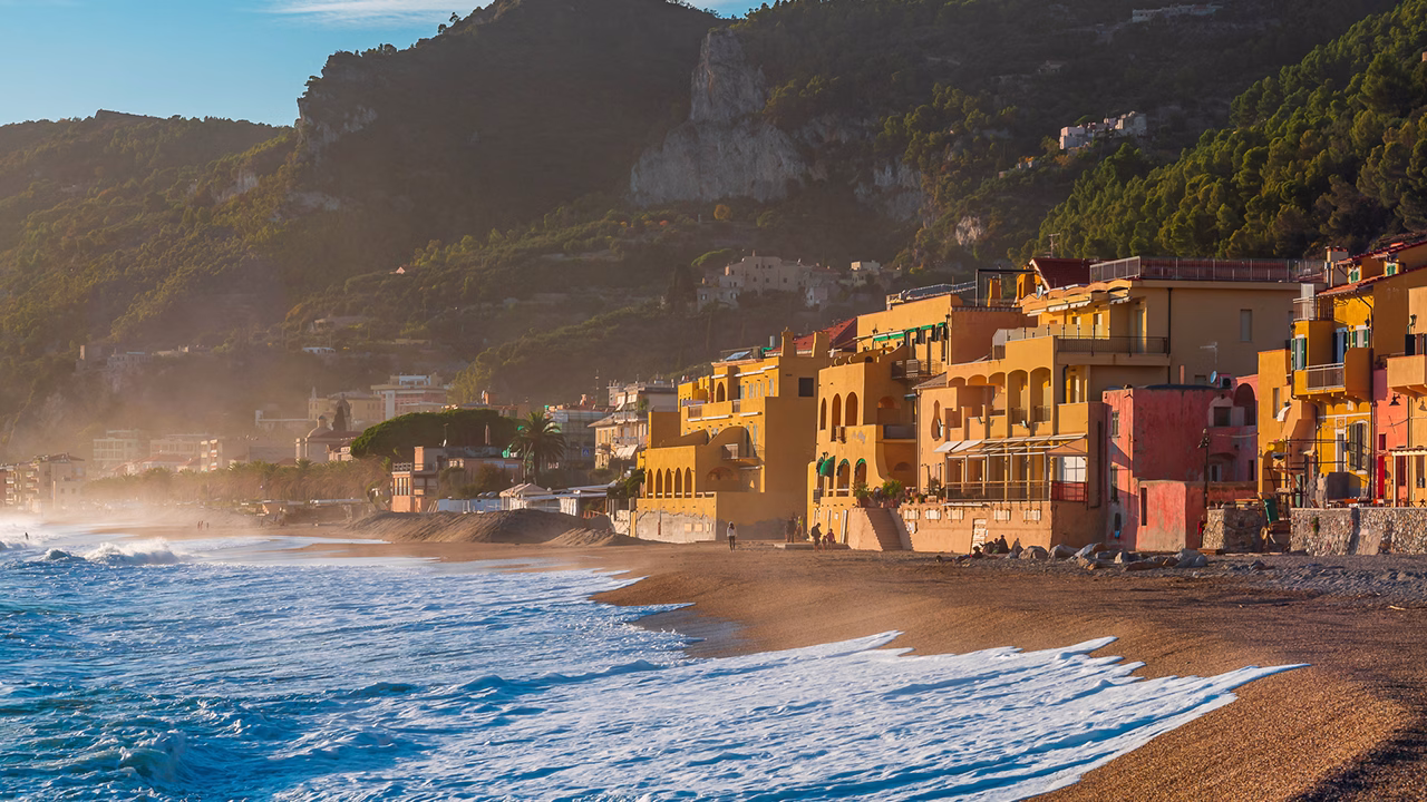 Spiaggia di Varigotti in Liguria al tramonto autunnale con le onde che si infrangono sulla riva e le tipiche case colorate sullo sfondo, meta ideale per viaggi gay in Italia.