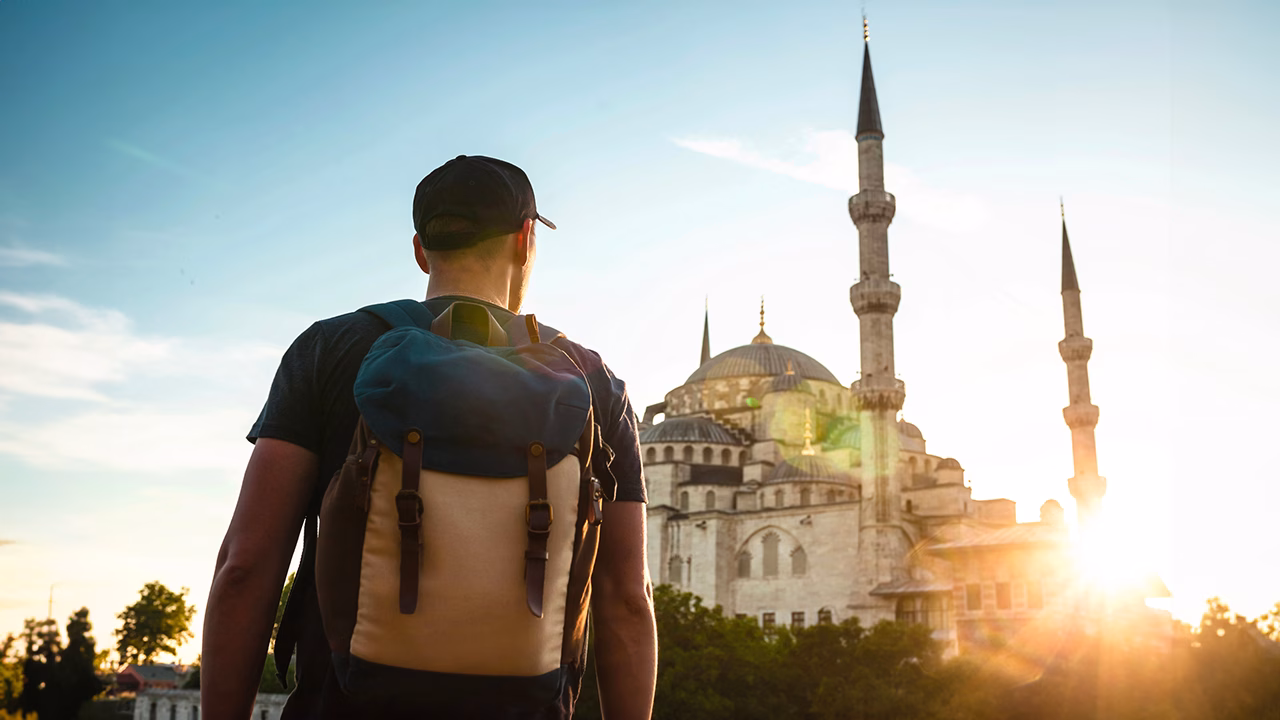 Viaggiatore gay con zaino in spalla ammira la Moschea Blu di Istanbul al tramonto, simbolo della citt&agrave; e meta imperdibile per un itinerario LGBTQ+ in Turchia.