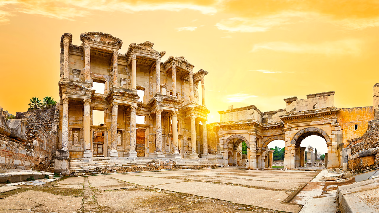 Panorama della Biblioteca di Celso tra le rovine dell&rsquo;antica citt&agrave; di Efeso a Izmir, illuminata dalla calda luce del tramonto che evidenzia l&rsquo;architettura romana e le maestose colonne in marmo.