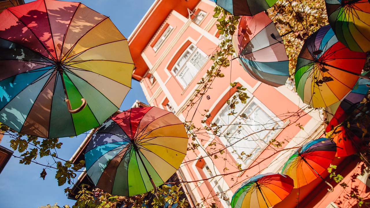 Colorati ombrelli arcobaleno sospesi sopra una via del quartiere LGBTQ+ di Kadık&ouml;y a Istanbul, simbolo di inclusivit&agrave; e creativit&agrave; urbana nella citt&agrave; turca.