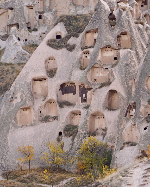 Parete rocciosa della Cappadocia punteggiata di antiche abitazioni scavate nella pietra, con finestrelle quadrate e aperture che testimoniano l&rsquo;architettura troglodita della regione.