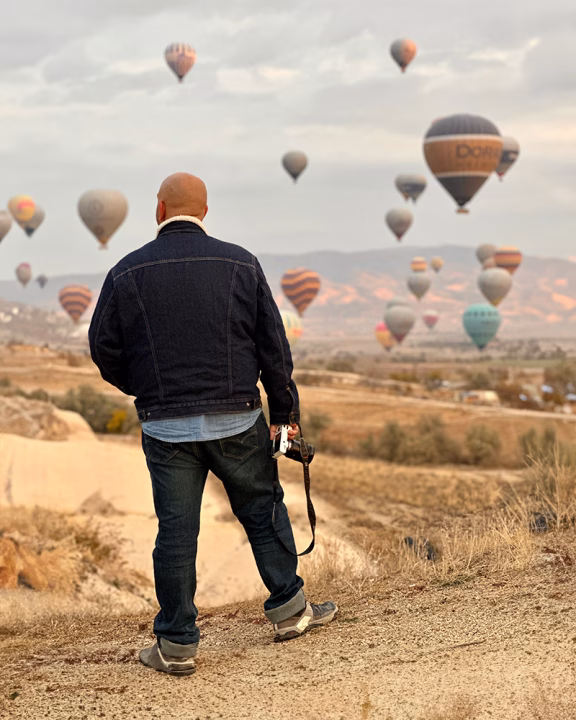 Daniele di Gayly Planet mentre osserva decine di mongolfiere colorate sorvolare il cielo della Cappadocia, immerso nel paesaggio montuoso al tramonto