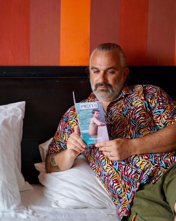 Luigi di Gayly Planet rilassato sul letto mentre sfoglia il welcome booklet del Men&rsquo;s Resort & Spa, l&rsquo;hotel gay-only di Siem Reap noto per accoglienza e comfort LGBTQ+.
