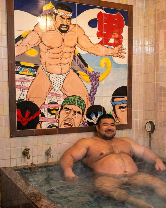 Uomo bear rilassato nella vasca calda di 24 Kaikan Asakusa a Tokyo, sauna gay in stile sentō con murale tradizionale giapponese